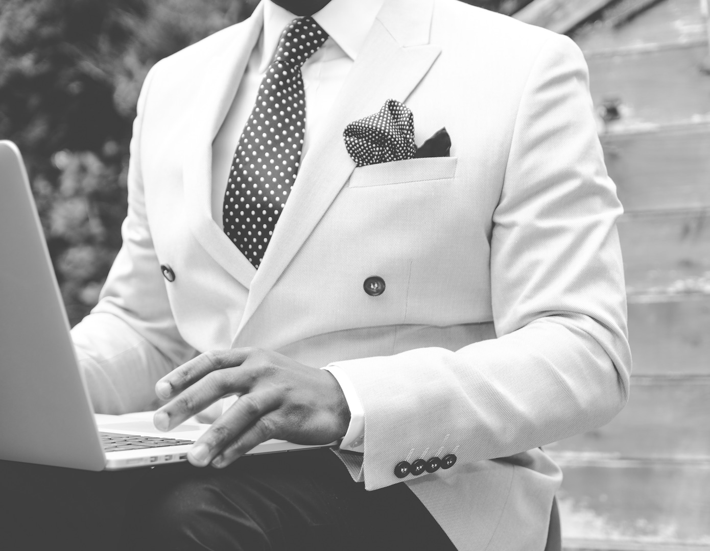 Black and white picture of a man in a suit sitting outside working on a laptop
