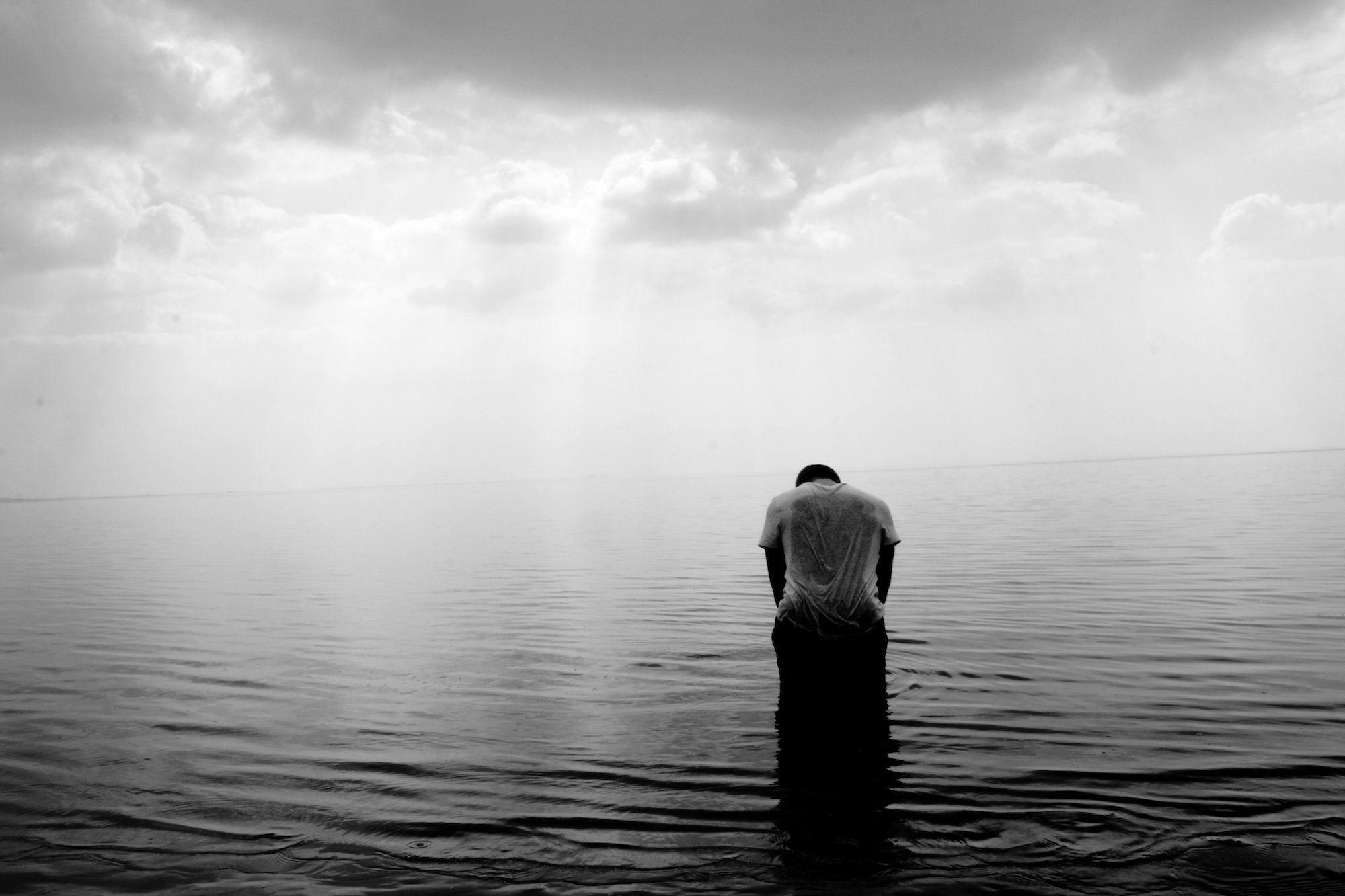 Man hunched over standing in a large body of water