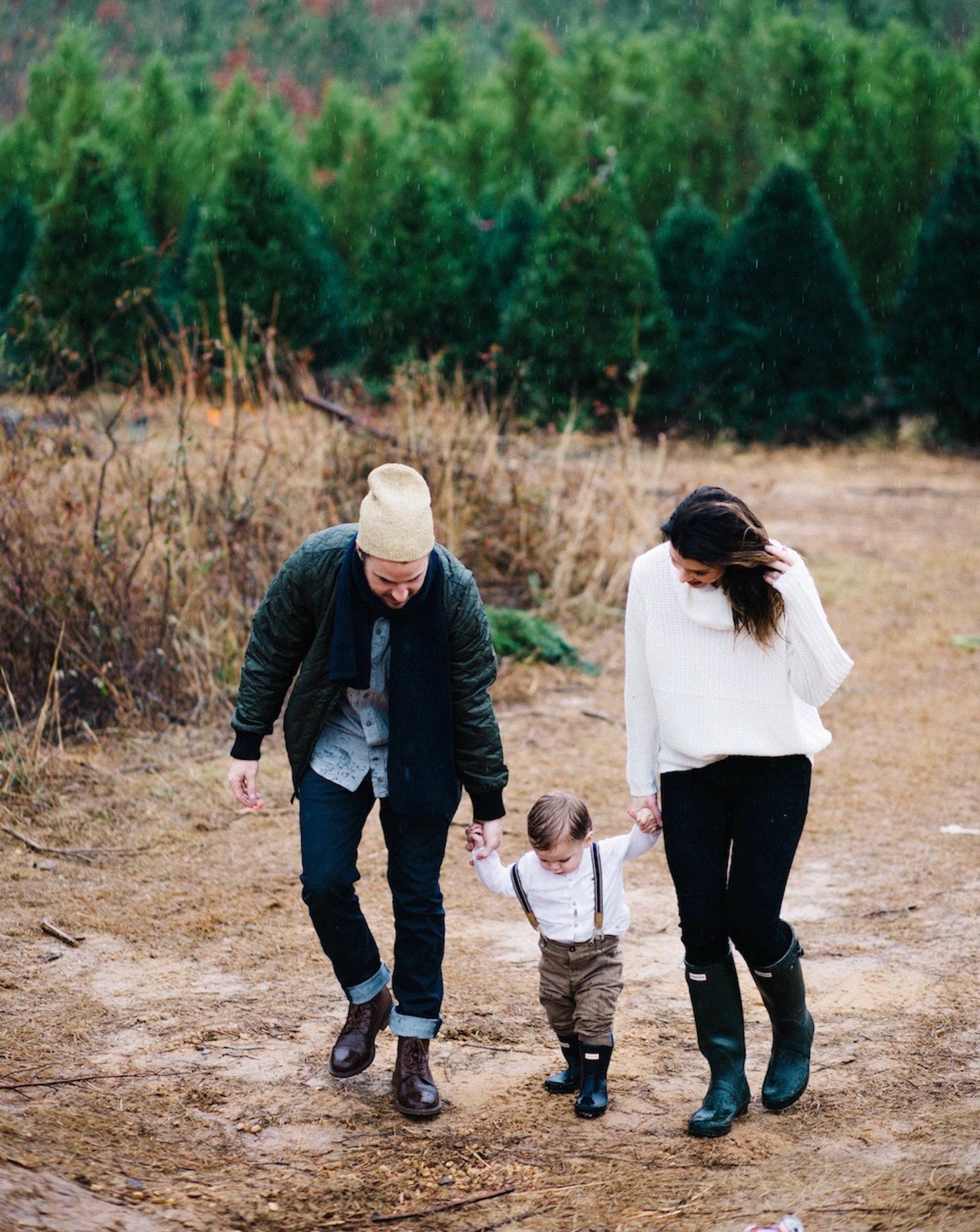 Mother and father on opposite sides of a young child, holding his hand and helping him walk.