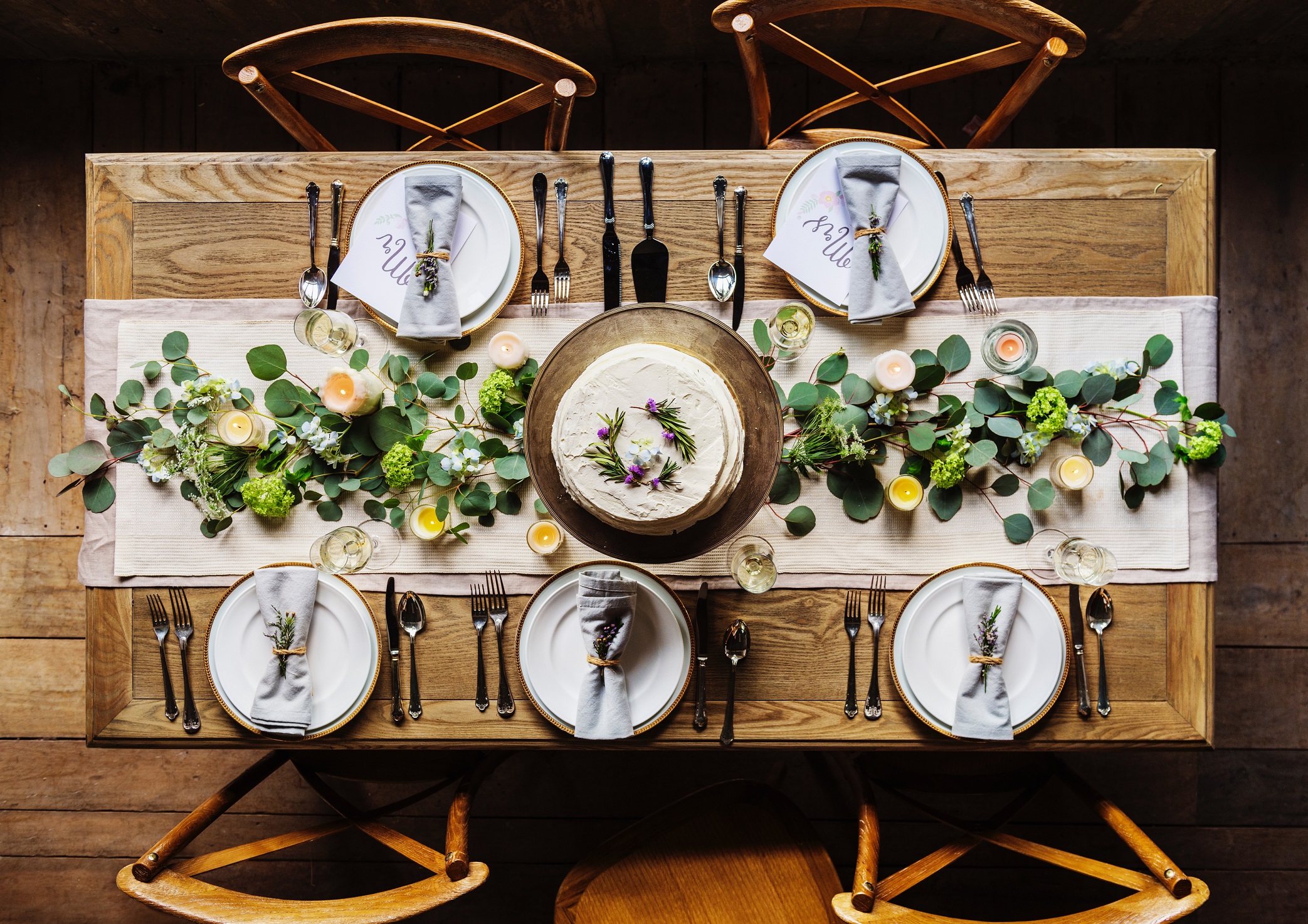 Table with four chairs, a vine placed in the middle, and five place settings that seem to be decorated for a wedding reception.